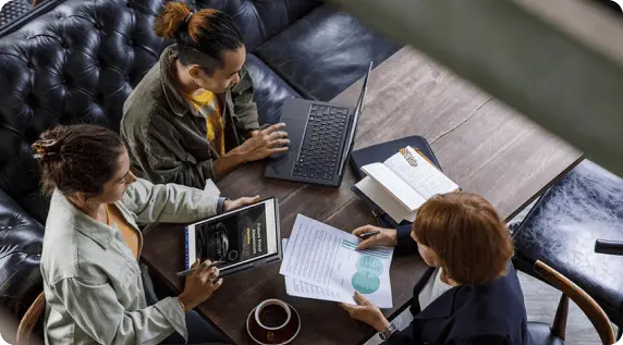 三個人坐在桌旁的俯視圖，其中一人正在查看文件，一人正在使用 Lenovo 平板電腦，還有一人正在使用 Lenovo 筆記型電腦。